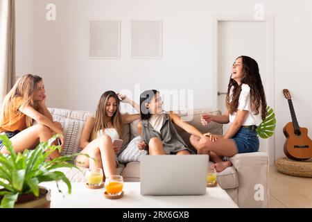 Amis assis sur le canapé avec ordinateur portable et riant à la maison Banque D'Images