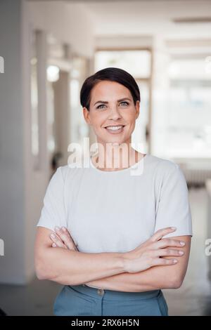 Femme d'affaires heureuse avec les bras croisés debout dans le lieu de travail Banque D'Images