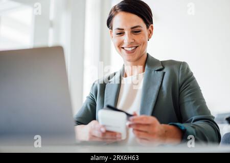 Femme d'affaires souriante utilisant la carte de crédit sur le lieu de travail Banque D'Images