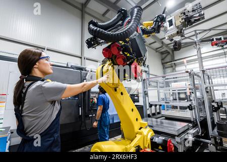 Technicien contrôlant le bras robotisé avec un collègue utilisant des machines en arrière-plan Banque D'Images