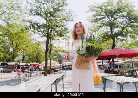 Femme souriante tenant la bouteille d'eau et l'épicerie dans le marché fermier Banque D'Images