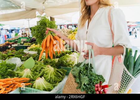 Femme achetant bouquet de carottes sur le marché Banque D'Images