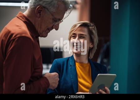 Femme d'affaires heureuse avec tablette PC parlant à un collègue au lieu de travail Banque D'Images