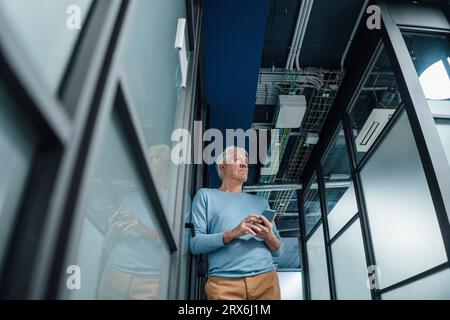Homme d'affaires contemplatif avec téléphone portable dans le bureau Banque D'Images