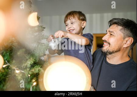 Père et fils souriants décorant l'arbre de Noël à la maison Banque D'Images