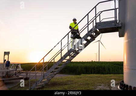 Ingénieur se déplaçant sur des marches par le champ avec des éoliennes Banque D'Images