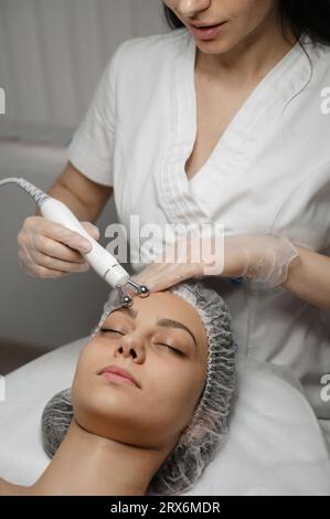 Jeune dermatologue massant avec de l'équipement sur le front de la femme Banque D'Images