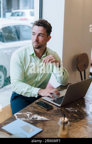 Homme d'affaires réfléchi assis avec ordinateur portable dans le café Banque D'Images