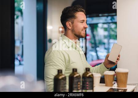 Jeune homme d'affaires souriant avec téléphone intelligent dans le café Banque D'Images