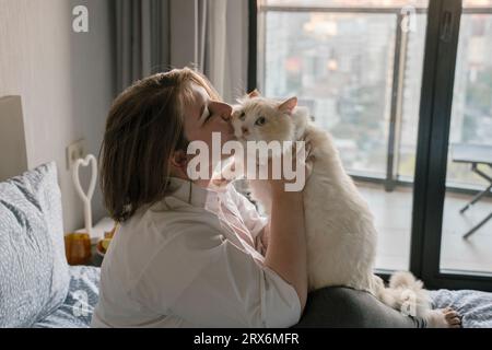 Jeune femme embrassant le chat sur le lit à la maison Banque D'Images