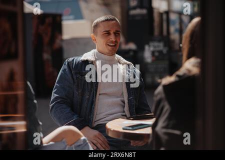 Bel homme parlant à ses meilleurs amis tout en étant assis au café dans la ville Banque D'Images