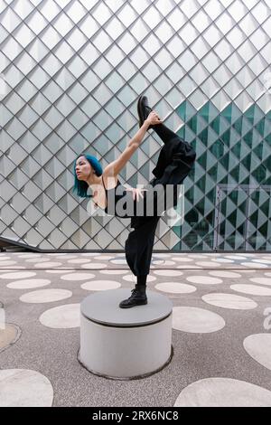 Jeune danseur flexible dansant sur un siège en béton circulaire devant un bâtiment moderne Banque D'Images