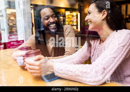 Heureux couple multiracial assis avec des tasses à café dans le café Banque D'Images