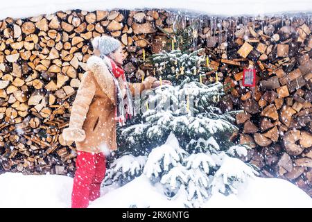 Femme senior décorant l'arbre de Noël devant des bois de feu Banque D'Images