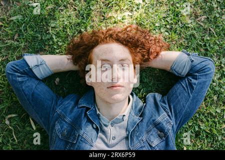 Young man with hands behind head lying on grass Banque D'Images