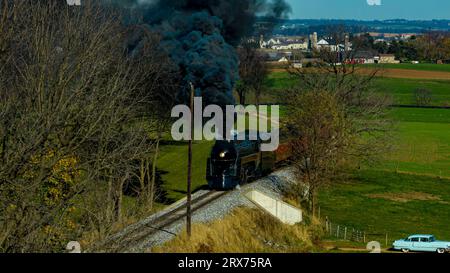 Une vue aérienne d'un train de passagers à vapeur profilé voyageant à travers des terres agricoles fertiles soufflant de la fumée noire un jour d'automne Banque D'Images