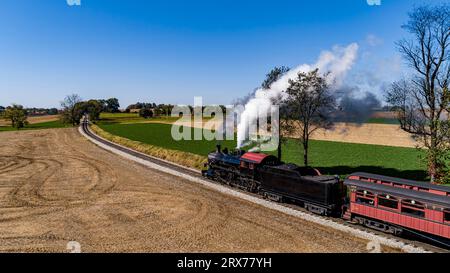 Un Drone vue latérale d'un train de passagers à vapeur antique, arrondissant une courbe, soufflant de la fumée, un jour d'automne ensoleillé Banque D'Images