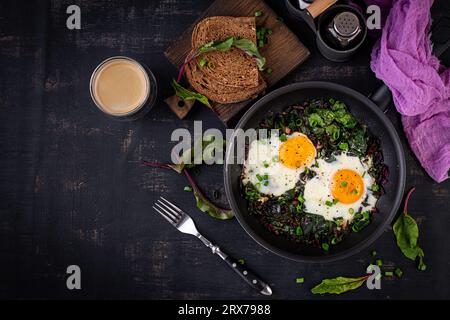 Petit déjeuner. Œufs frits avec feuilles de betterave verte, ail, poivre et oignon vert dans une poêle. Vue de dessus, pose à plat Banque D'Images