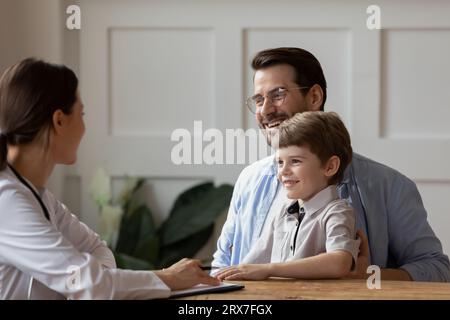 Petit garçon souriant assis sur des genoux de père, pédiatre en visite Banque D'Images