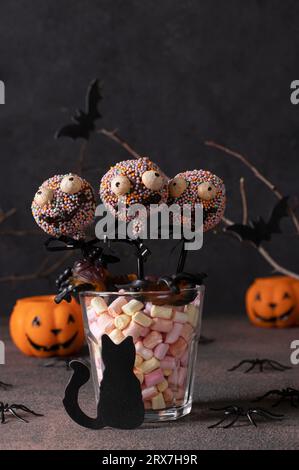 Gâteau d'Halloween maison pop monstres avec chocolat noir sur fond gris. Bonbons pour les enfants sur la fête d'Halloween Banque D'Images