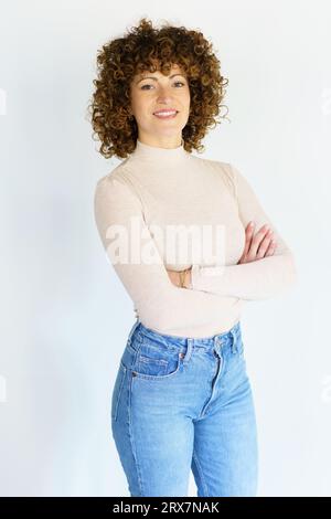 Femme aux cheveux bouclés souriante avec les mains croisées Banque D'Images