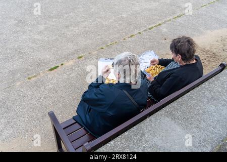 Deux personnes assises sur un banc à l'extérieur, vues d'en haut, mangent du Fish and chips pour le déjeuner du vendredi sur le Fish Quay, North Shields, North Tyneside, Royaume-Uni Banque D'Images