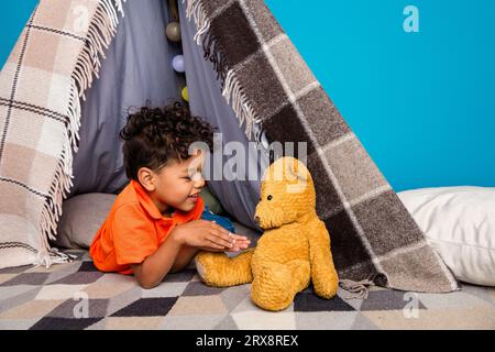 photo de petit enfant dans la tente diy jouant parlant avec l'ours en peluche doux ours en peluche isolé fond de couleur bleue Banque D'Images