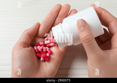 Femme versant des pilules de la bouteille sur la main à la table en bois blanc, closeup Banque D'Images