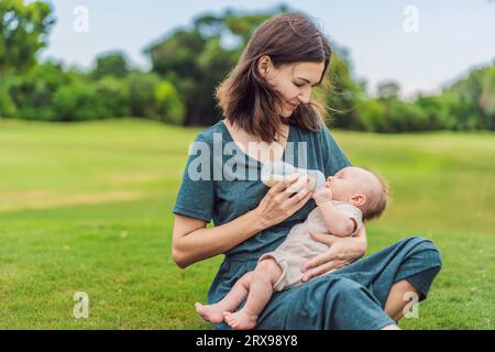 Mère tenant et nourrissant le bébé du biberon dans le parc. Portrait de bébé nouveau-né mignon étant nourri par sa mère en utilisant le biberon. Femme aimante donnant Banque D'Images