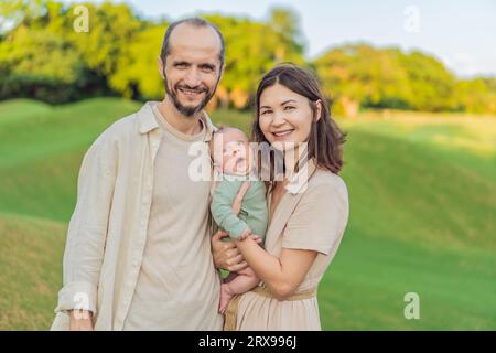 Un heureux couple de 40 ans berce son nouveau-né dans un parc baigné de soleil. Amour, famille et générations en harmonie Banque D'Images