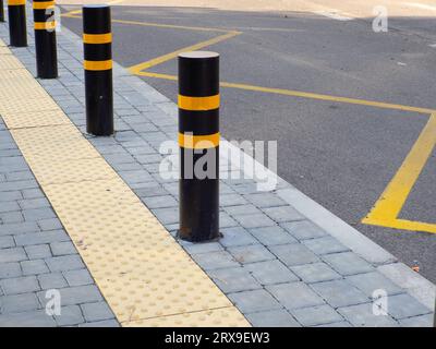 Trottoir tactile jaune pour les aveugles sur l'arrêt de bus. Arrêt de bus avec bornes de circulation protégeant le trottoir piéton. Concept de restriction de trafic Banque D'Images