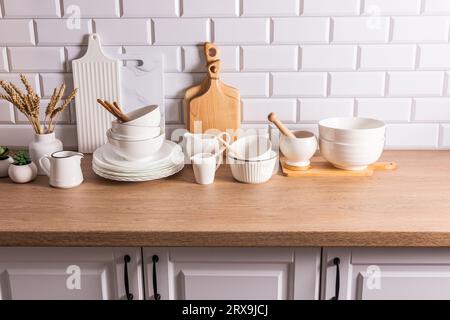 Ustensiles en céramique blanche et ustensiles de cuisine sur un comptoir en bois dans une cuisine écologique avec des plantes d'intérieur vertes. Maison confortable. Banque D'Images