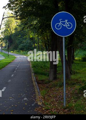 Vue sur le panneau routier et piste cyclable dans le parc avec espace de copie. Entre les arbres du parc il y a une piste cyclable bordée de panneaux et mar Banque D'Images