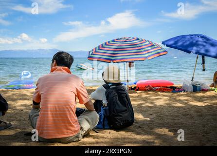 Touristes assis sur la plage de sable de Pope Beach. Des gens méconnaissables qui s'amusent dans l'eau. South Lake Tahoe. Banque D'Images