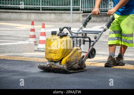 Opérateur lavant l'asphalte sur la rue avec rouleau automatique jaune Banque D'Images