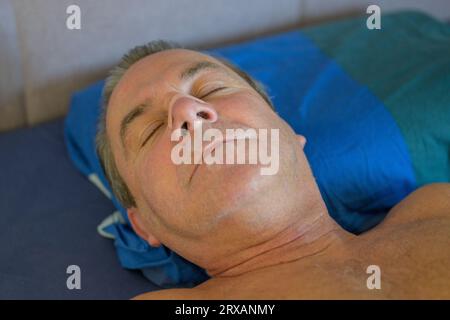 Gros plan d'un homme d'âge moyen endormi avec une bande nasale et une bande buccale couchée dans son lit Banque D'Images