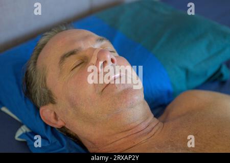 Gros plan d'un homme d'âge moyen endormi avec une bande nasale et une bande buccale couchée dans son lit Banque D'Images