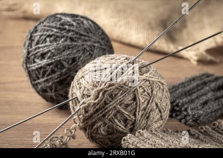 Des boules de fil gris fait maison et des aiguilles à tricoter et des articles tricotés reposent sur la table Banque D'Images