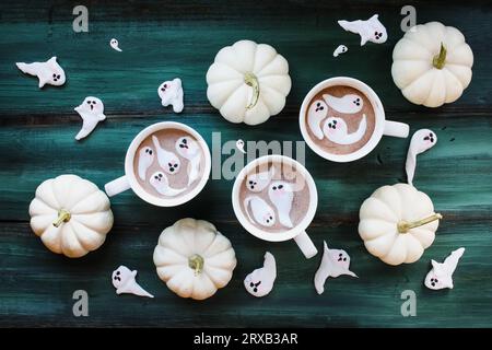 Chocolat chaud Halloween avec fantôme mignon de guimauve avec des visages effrayants. Vue de dessus de table avec fond vert rustique. Banque D'Images