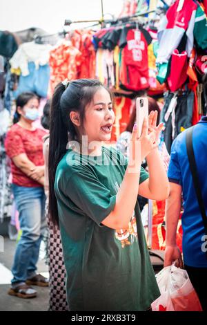 Un joli détenteur de stalle de marché thaïlandais enregistre les vêtements sur son stand au marché de Pratu Nam, Bangkok, Thaïlande. Banque D'Images