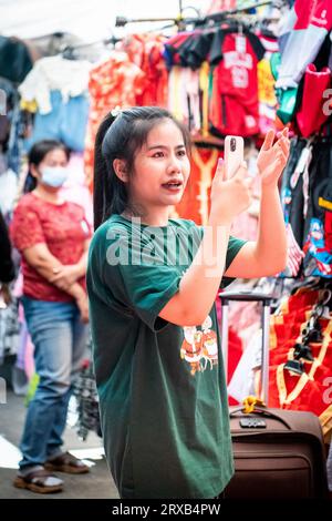 Un joli détenteur de stalle de marché thaïlandais enregistre les vêtements sur son stand au marché de Pratu Nam, Bangkok, Thaïlande. Banque D'Images