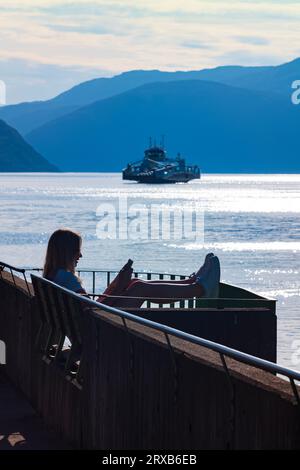 Fodness, Norvège, 24 juin 2023 : silhouette d'une femme sur un téléphone intelligent attendant le ferry Fodnes-Mannheller pendant une soirée d'été. Il y en a 18 Banque D'Images