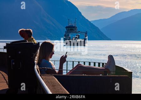 Fodness, Norvège, 24 juin 2023 : silhouette d'une femme sur un téléphone intelligent attendant le ferry Fodnes-Mannheller pendant une soirée d'été. Il y en a 18 Banque D'Images