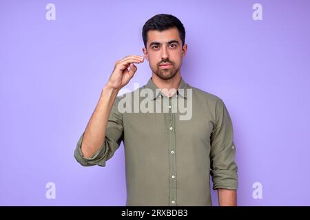 Homme barbu sérieux confiant en chemise verte montrant la lettre D symbole de langue des signes pour l'homme sourd avec fond bleu. isolé Banque D'Images