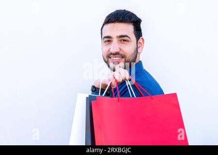 Jeune homme tenant des sacs à provisions sur fond isolé blanc pour les promotions de vendredi noir et blanc avec le visage joyeux Banque D'Images