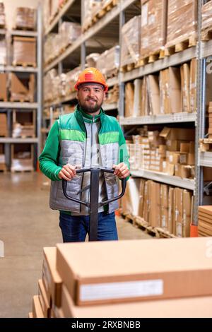 ouvrier d'entrepôt caucasien avec transpalette manuel, travaillant dans la salle de stockage, transportant des marchandises en carton, livraison de boîtes. logistique et distribution Banque D'Images