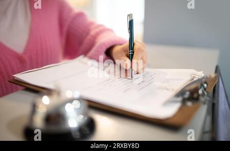 Photo recadrée de la femme signant le formulaire de remplissage de papiers à l'hôtel Banque D'Images