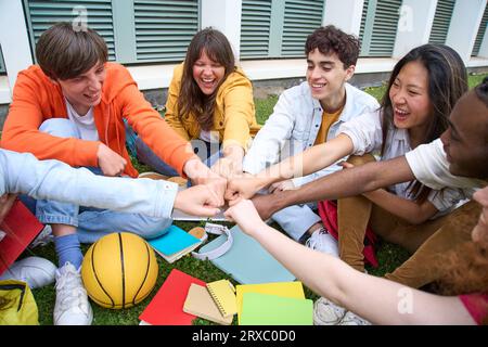 Divers jeunes amis réunis en cercle assis sur le campus excités poing cognant. Groupe multiethnique. Banque D'Images