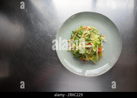 Une salade verte mixte est présentée sur une assiette rustique, placée sur une table en métal. Banque D'Images