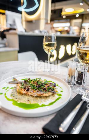 Bar en sauce crème aux herbes provençales et huile d'olive verte sur une assiette blanche sur une table en marbre dans un restaurant Banque D'Images